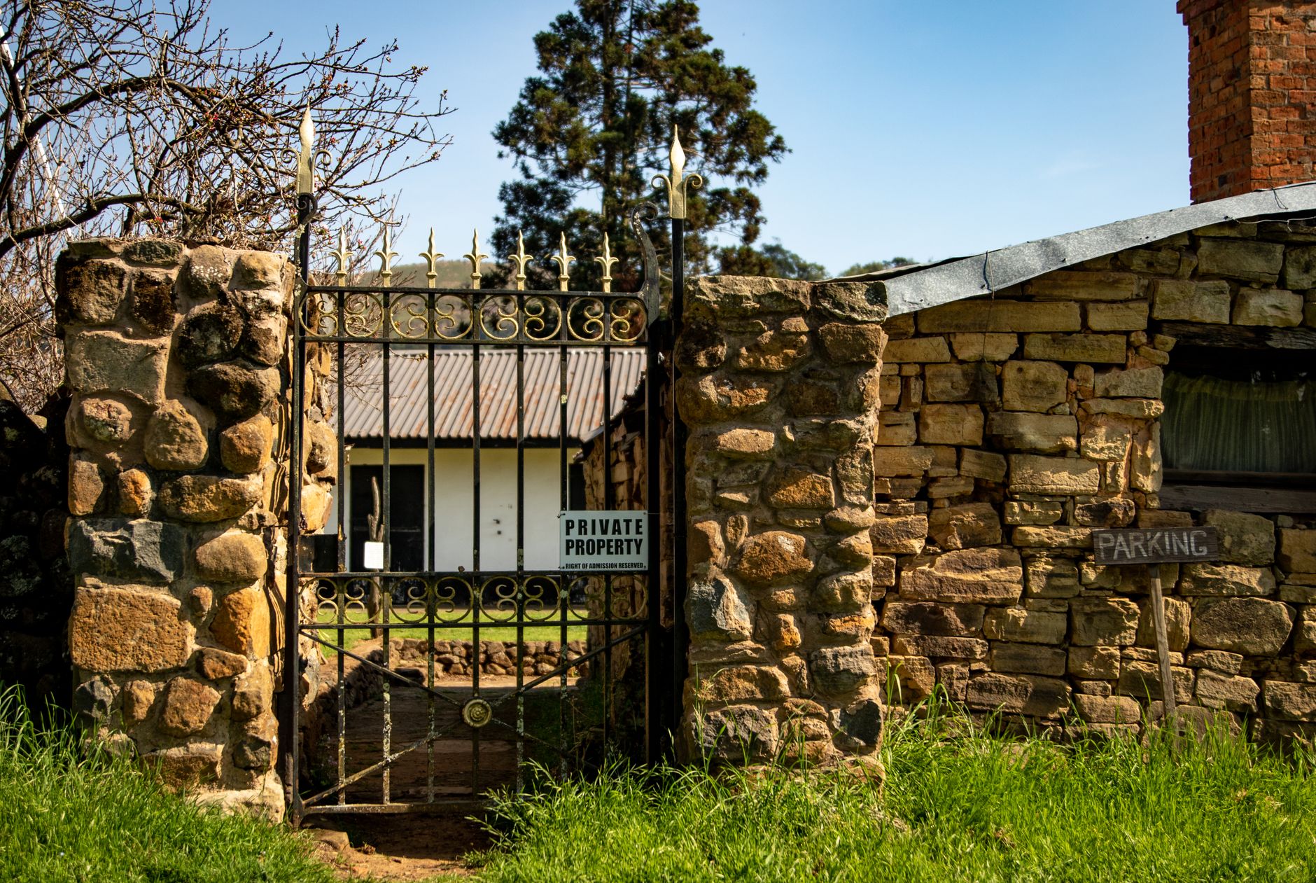 A rustic stone gate with metal accents leads to a private property surrounded by greenery