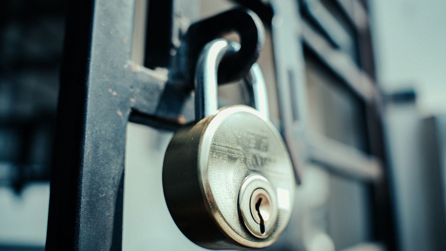 Padlock hanging through the latch hasp of a dark metal gate