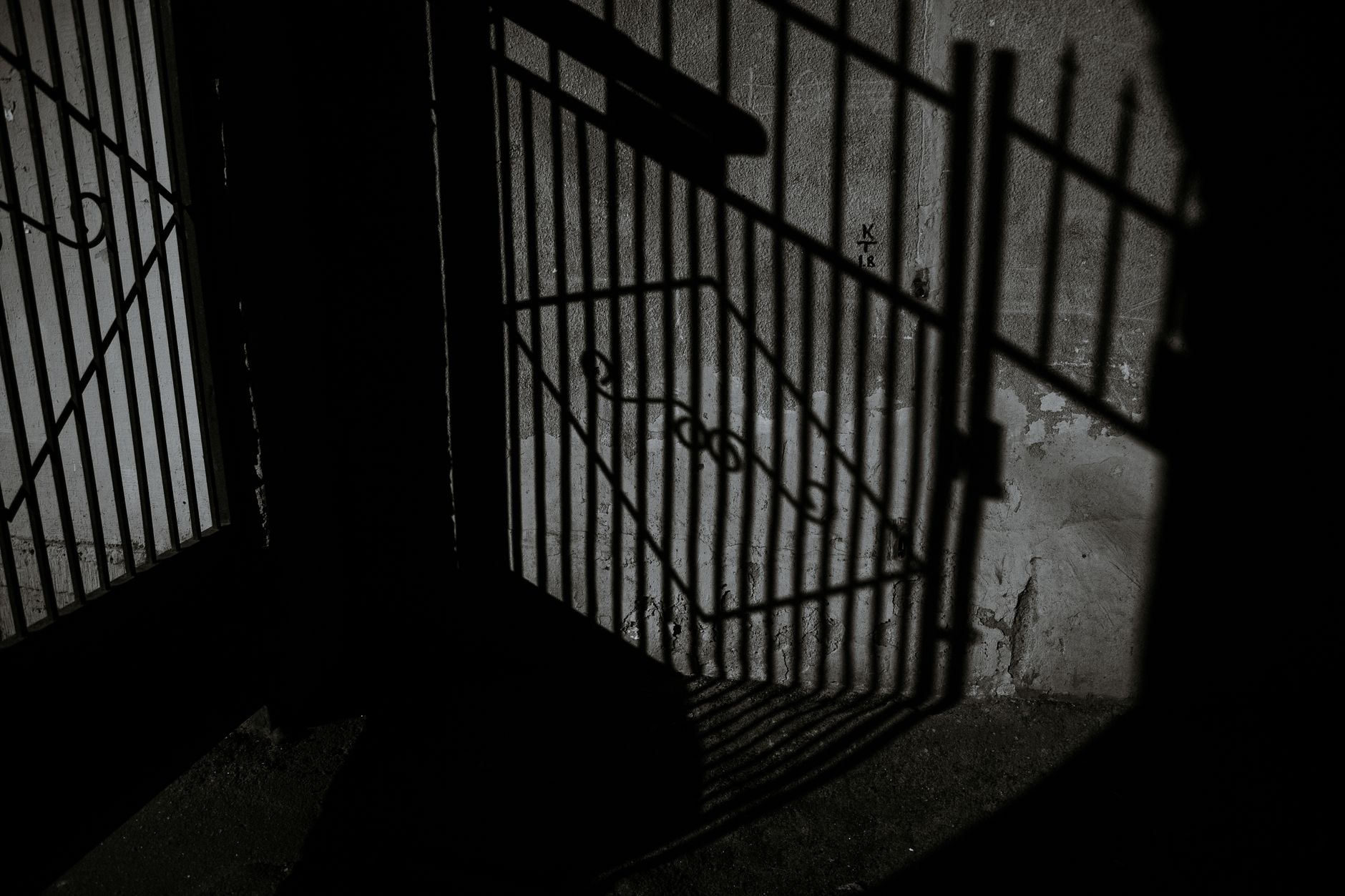 Black and white of aged concrete building exterior with sun shadow in form of metal gate decorated with